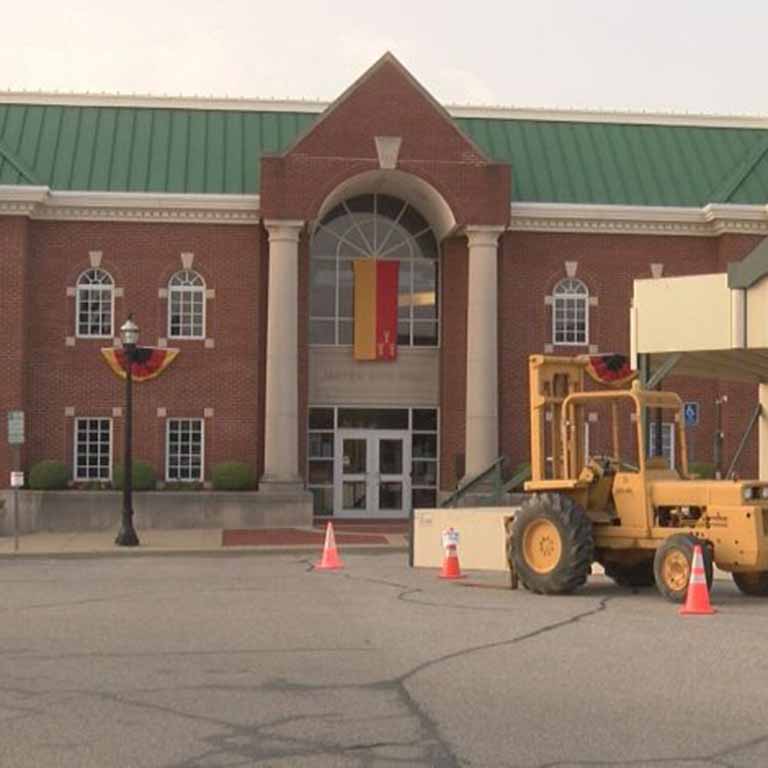 Big yellow construction vehicle in front of a brick government building.